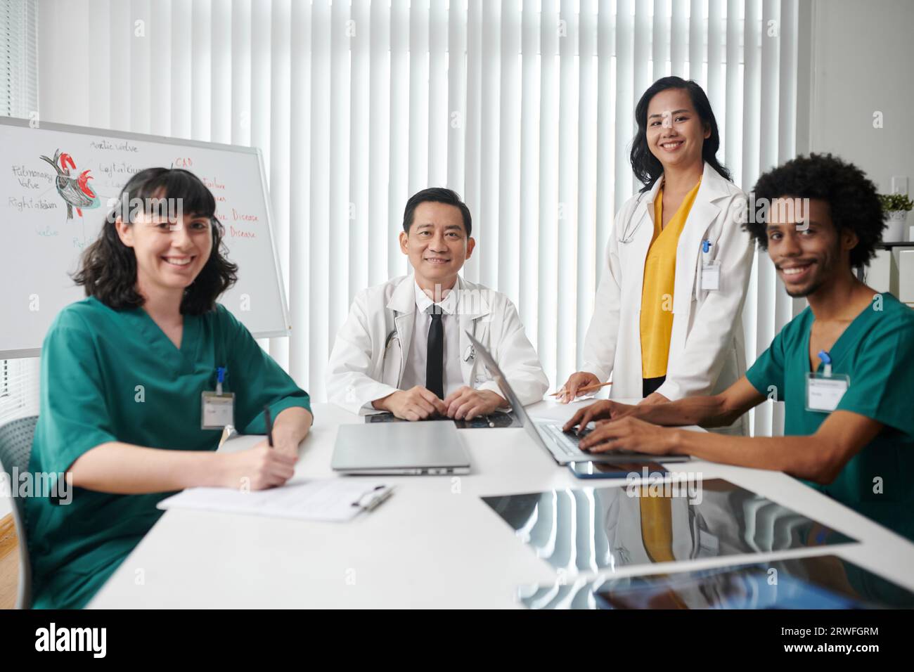 Felice team medico seduto a grande tavolo in ufficio di clinica Foto Stock