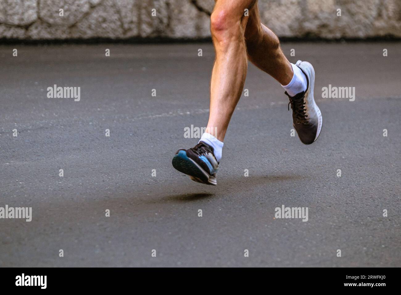 corridore maschile con gambe ravvicinate che corre su una maratona grigia di asfalto Foto Stock