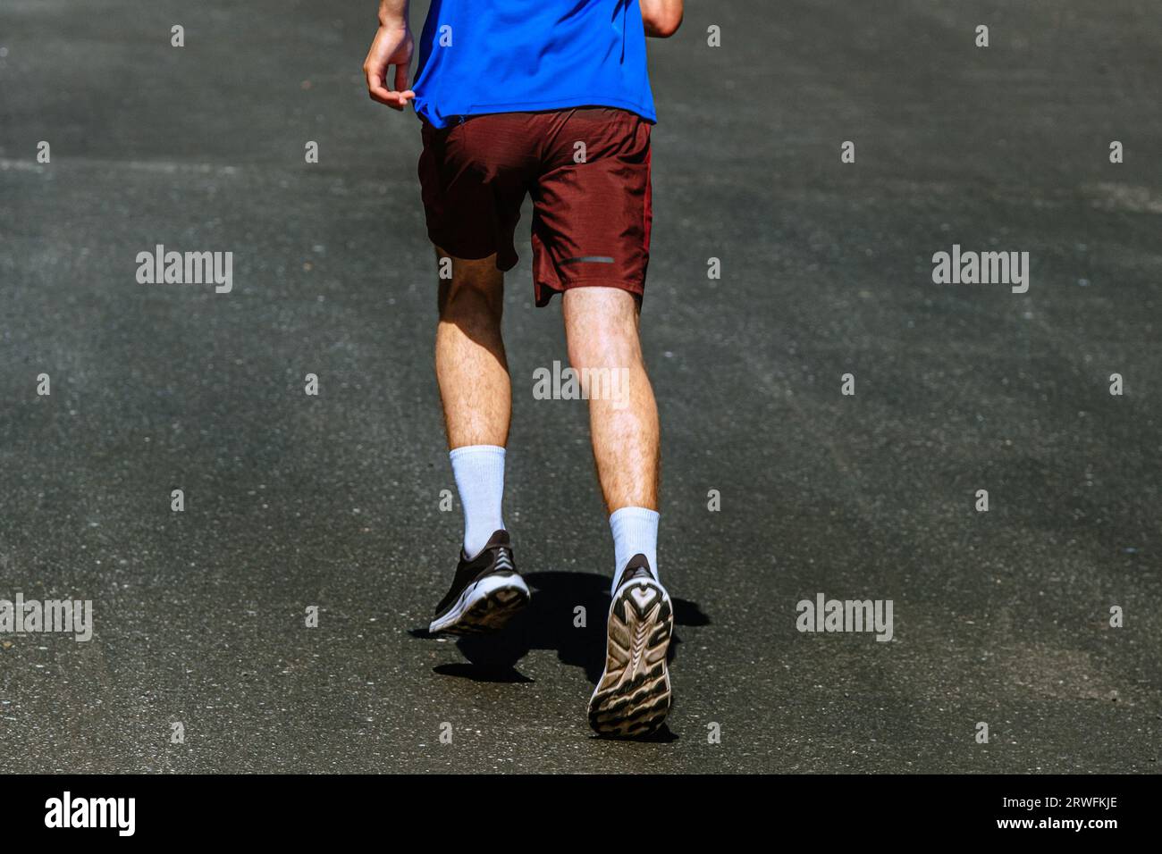 vista posteriore del corridore maschile che corre in salita su fondo asfalto scuro, gara di maratona estiva Foto Stock