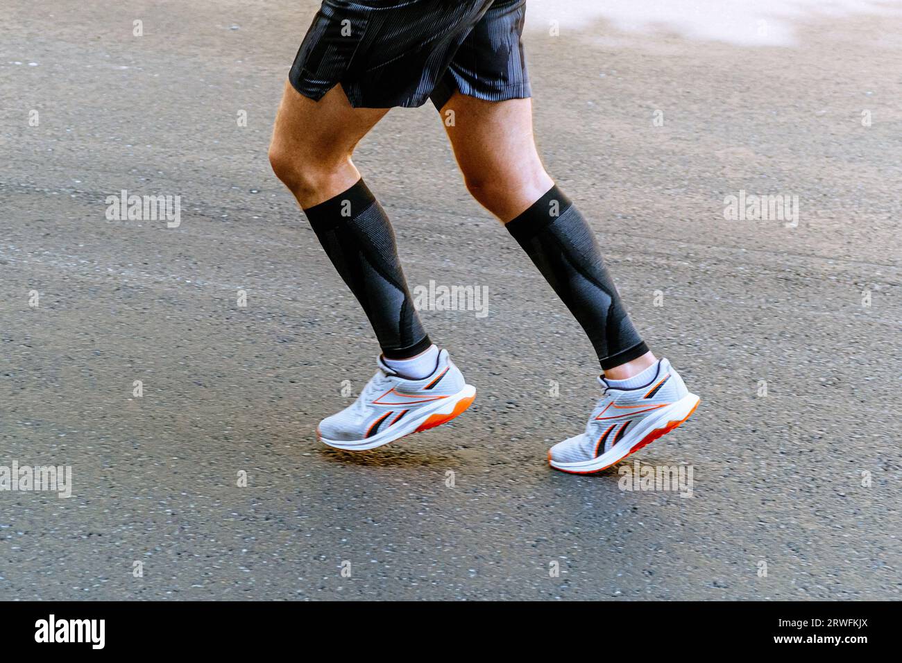 runner maschile con gambe a vista laterale in maniche a compressione che corre su maratona in asfalto grigio Foto Stock