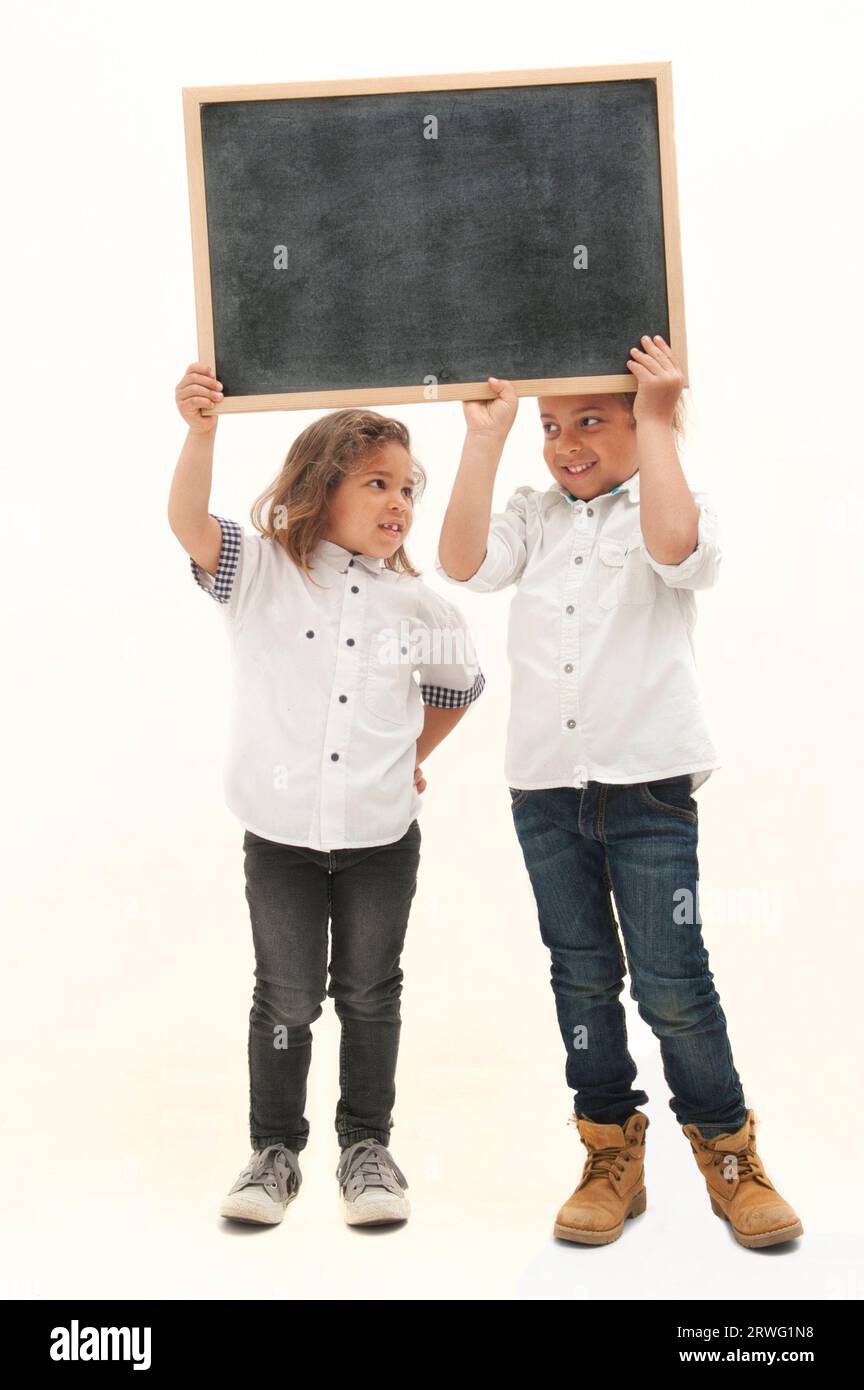 Inglese: Due bambini multietnici con i capelli lunghi tengono in mano una lavagna bianca su sfondo bianco Foto Stock