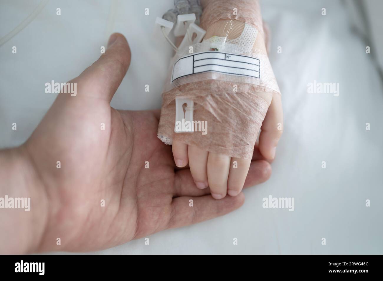 Il genitore tiene la mano del bambino con la vista ravvicinata del gocciolamento IV sullo sfondo del letto Foto Stock