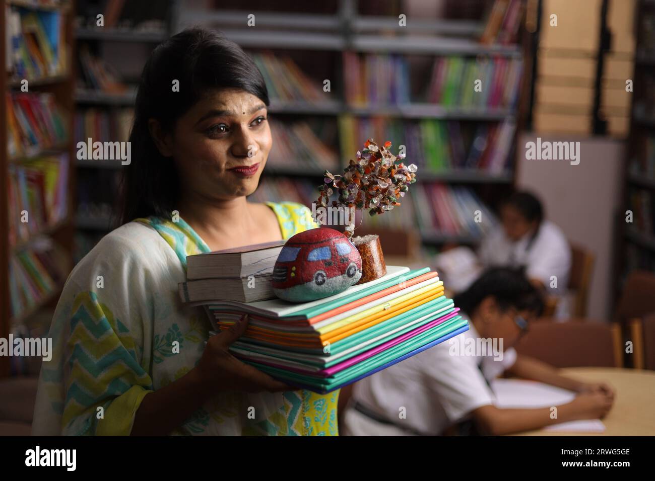 Insegnante indiana che tiene un pacchetto di libri nelle sue mani, in piedi in biblioteca, pressione di studio, forza educativa. Foto Stock