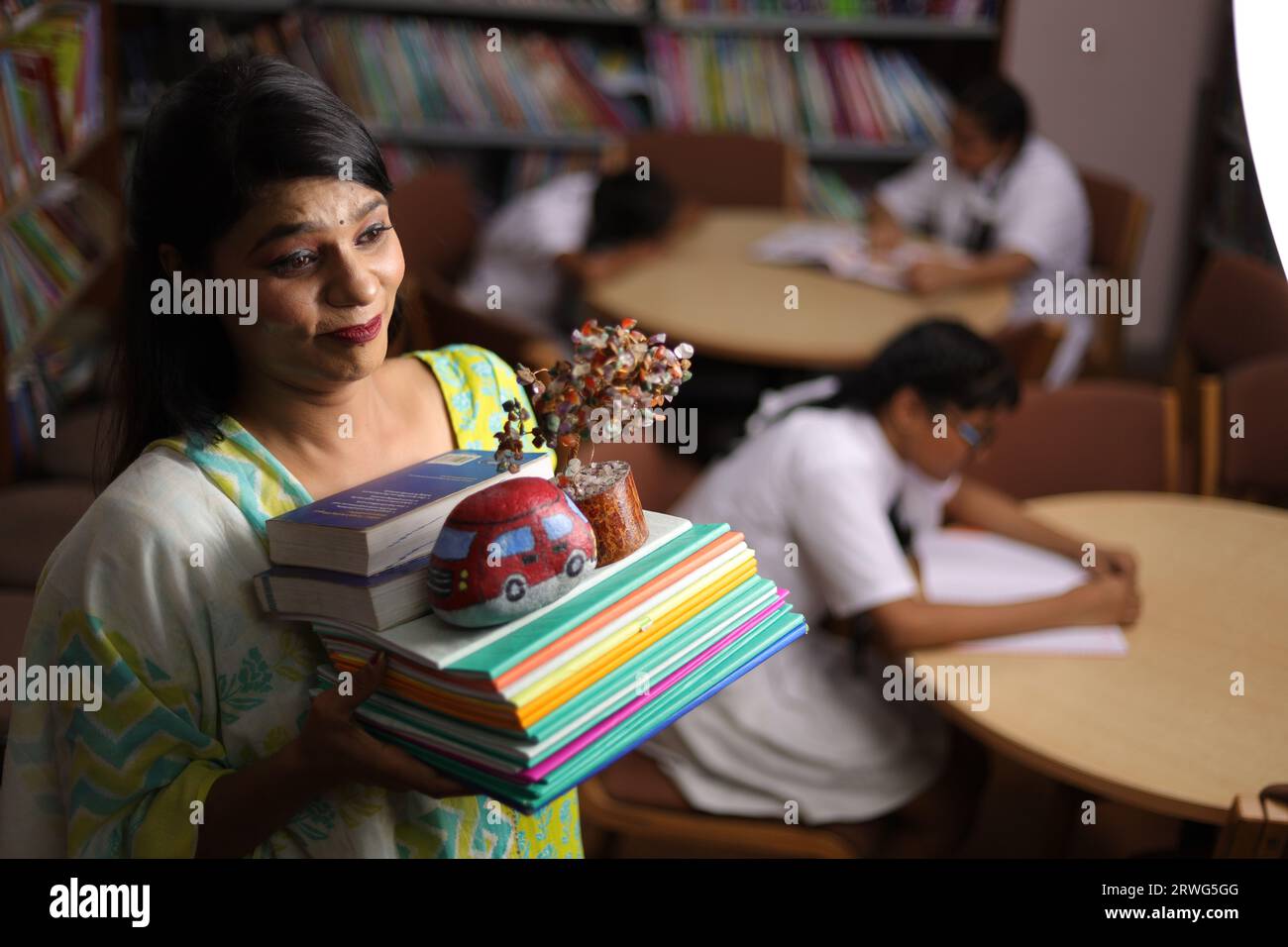 Insegnante indiana che tiene un pacchetto di libri nelle sue mani, in piedi in biblioteca, pressione di studio, forza educativa. Foto Stock
