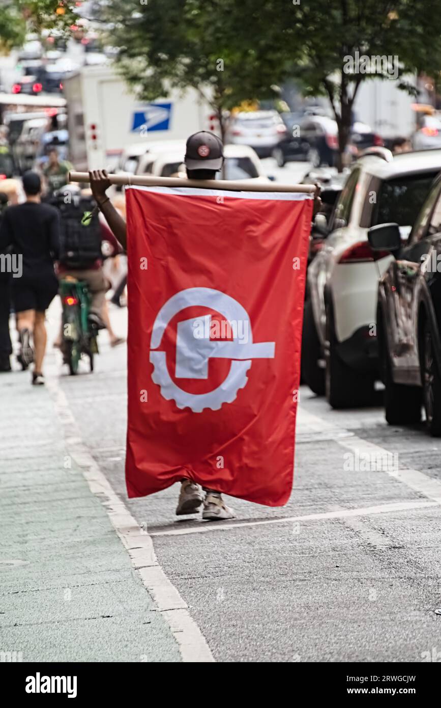New York, New York - 17 settembre 2023: La bandiera del Partito Comunista degli Stati Uniti è attaccata sul retro di un sostenitore afroamericano di colore in strada a New York. Foto Stock