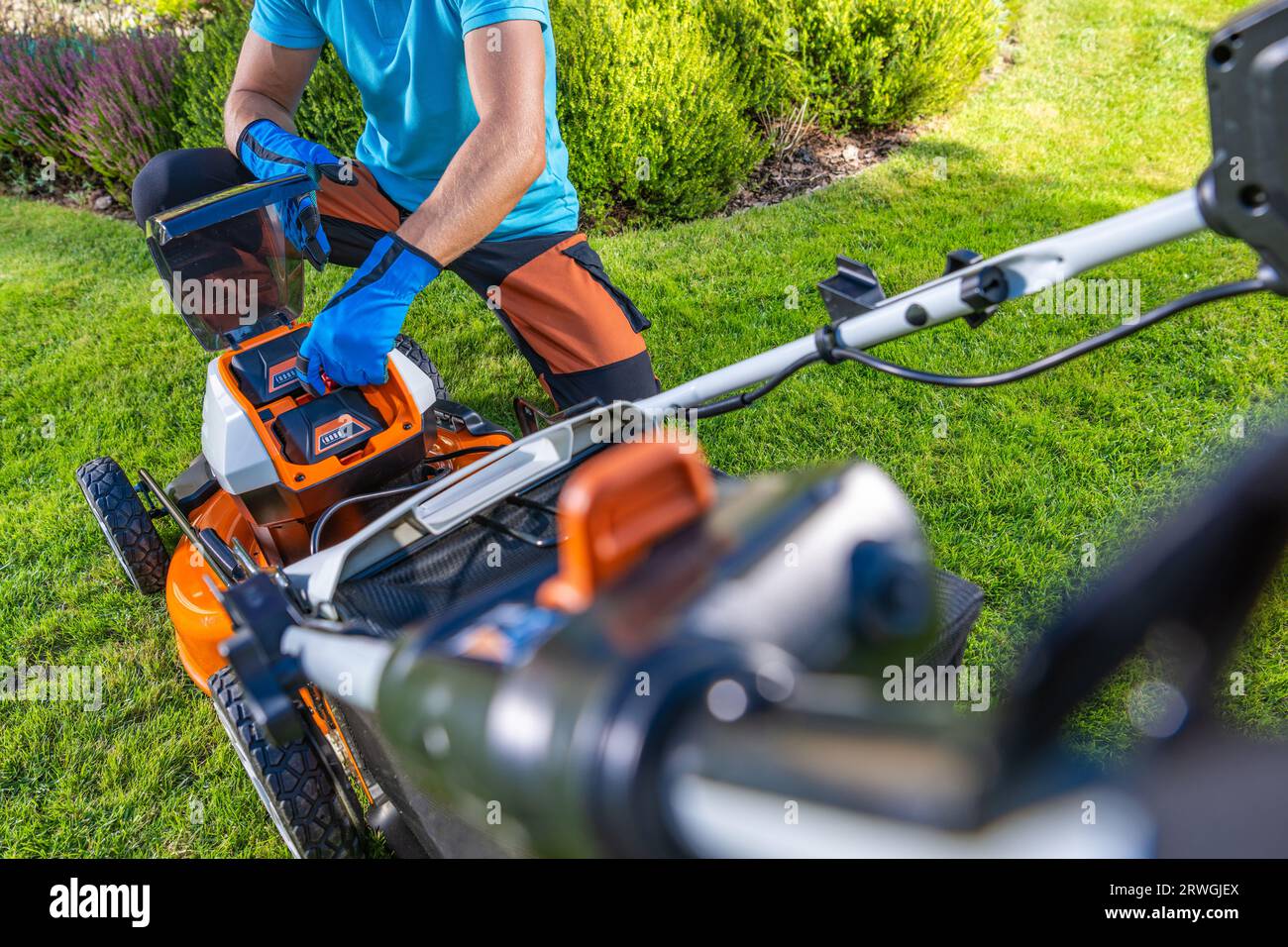 Proprietario di giardini che sostituisce le batterie all'interno della sua moderna falciatrice da erba elettrica cordless Foto Stock