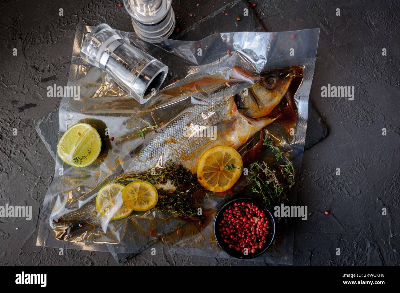 Pesce spigola fresco. Pesce spigola crudo con ingredienti speziati ed erbe aromatiche per cucinare su fondo di pietra nera. Vista dall'alto. Foto Stock