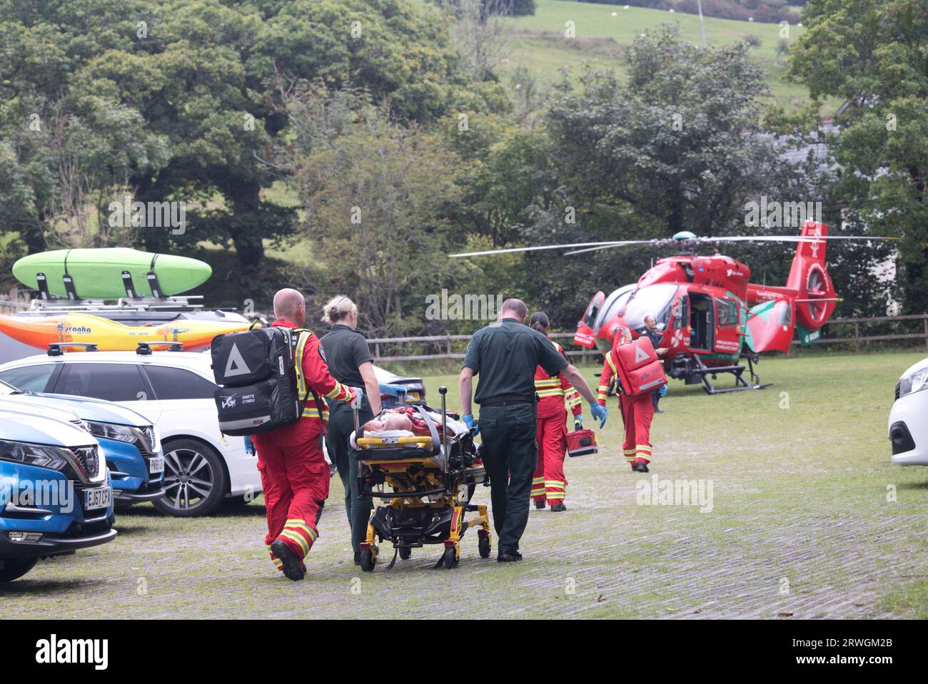 Squadra medica che porta motociclista ferito su tram a rosso Wales Helicopter ambulanza fuori National Whitewater Centre vicino Bala North Wales Foto Stock