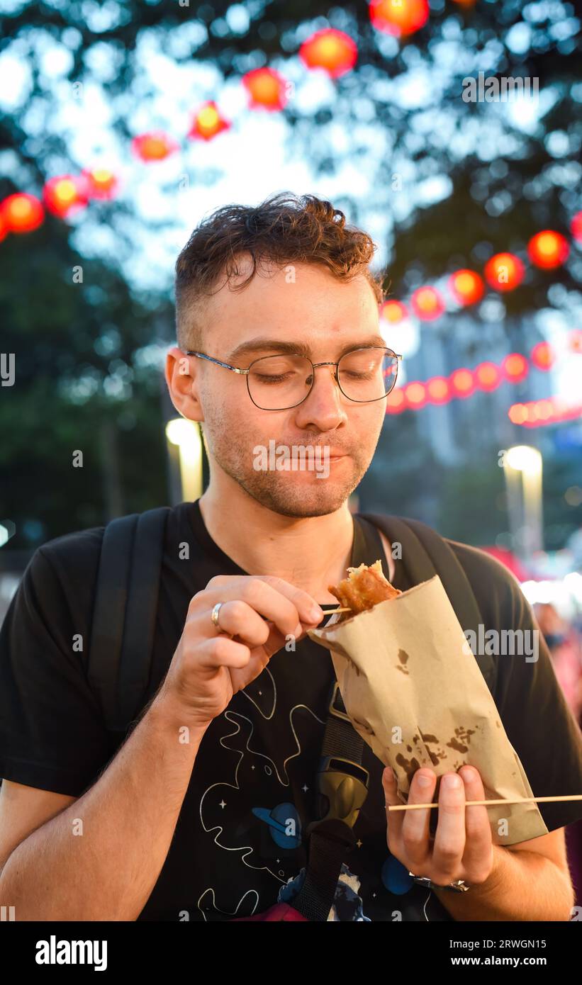 Giovane turista che mangia banana fritta a Jalan Alor Street food a Kuala Lumpur, Malesia Foto Stock