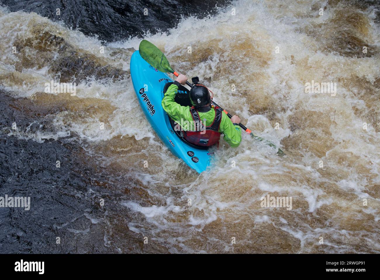 Canoista in slalom blu e giacca verde che cavalca le rapide in slalom Whitewater nel fiume Tryweryn presso il National Whitewater Centre vicino Foto Stock