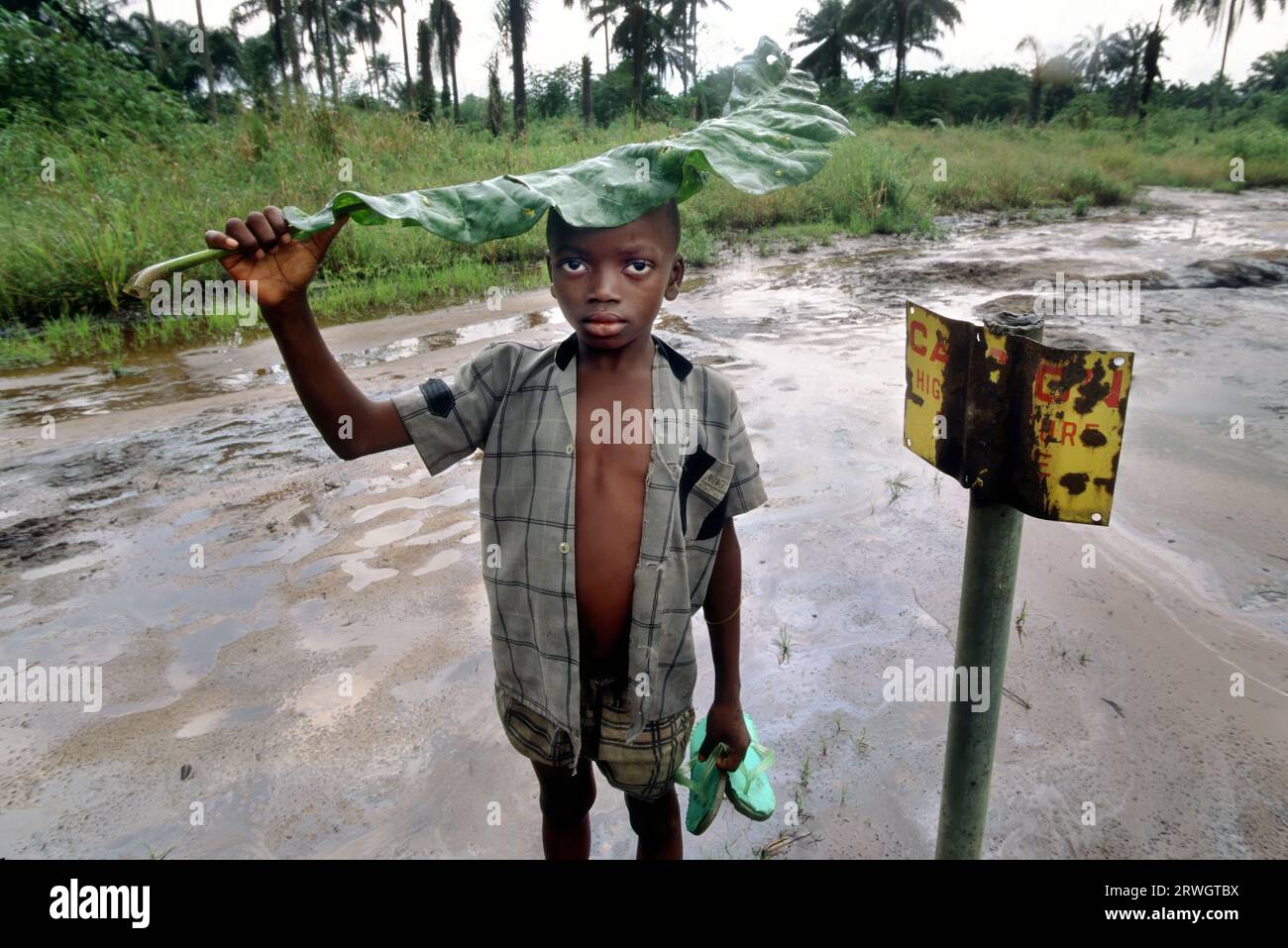 Nigeria: Un ragazzo si trova oltre a un segnale di pericolo da parte di una zona contaminata da petrolio a Ogoniland. Distruzione ambientale causata dalla fuoriuscita di petrolio greggio nella zona di produzione petrolifera del sud del paese, prevalentemente abitata dalla tribù Ogoni. Foto Stock