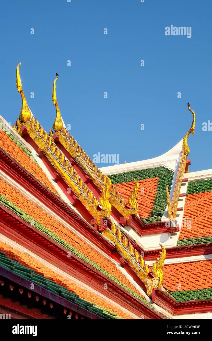 Tetto di un tempio in Thailandia. Il tetto è composto da più strati di piastrelle rosse e verdi, decorate con ornamenti dorati. Il cielo è blu chiaro. T Foto Stock