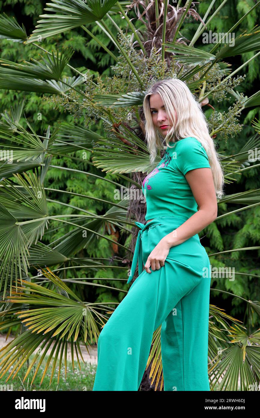 Donna bionda con capelli lunghi e vestito verde che posa in natura Foto Stock