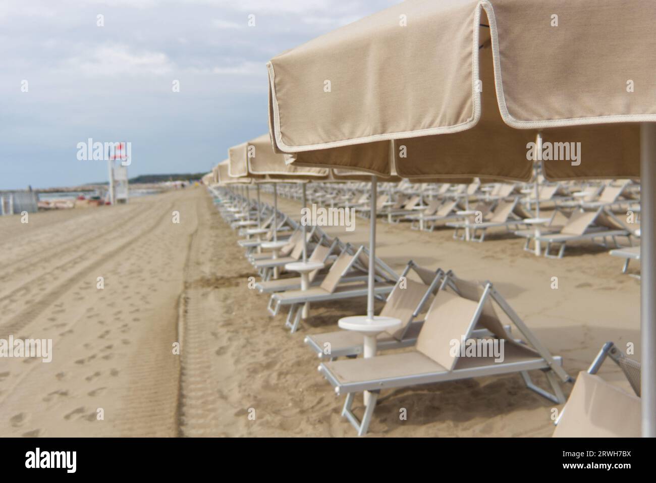 Un ombrellone beige con più ombrelloni e lettini allineati. Foto Stock