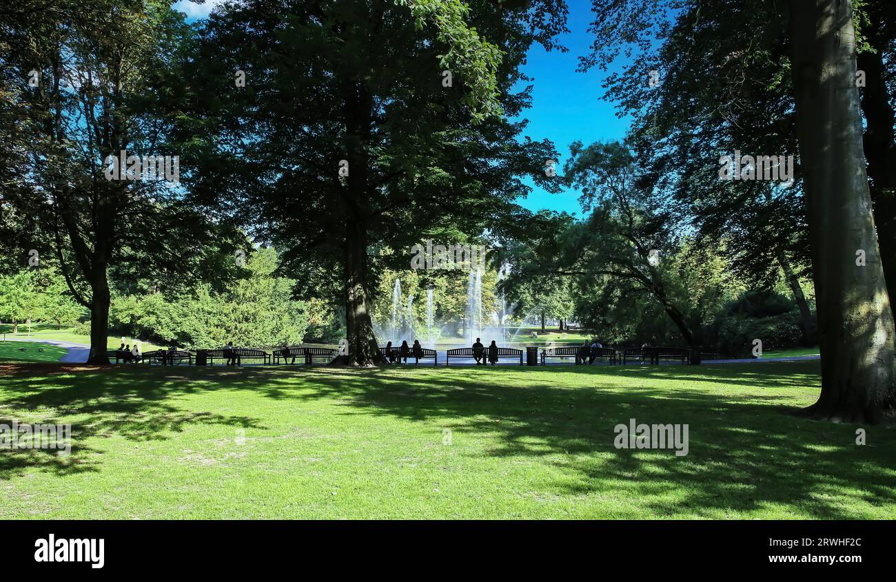 Breda, Paesi Bassi - agosto 30. 2023: Persone irriconoscibili sedute su panchine all'ombra degli alberi presso lo splendido stagno, fontana nel verde della città Foto Stock