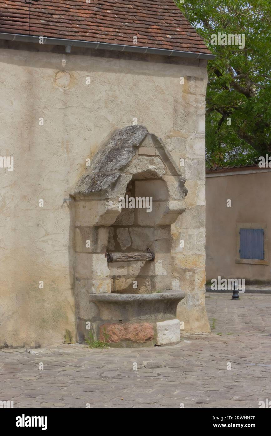 Vecchio pozzo contro una parete color crema in un villaggio francese Foto Stock