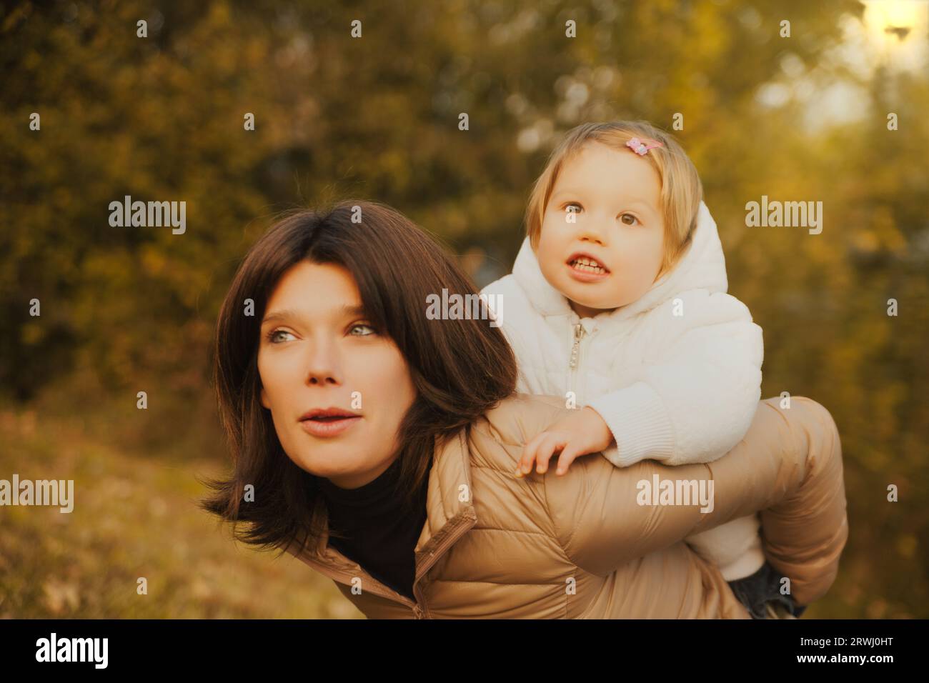 Godendosi l'aria aperta, un bambino biondo sale sulle spalle della sua adorabile madre. Sono entrambi vicini al freddo autunnale, condividendo una giornata di sconfinata Foto Stock