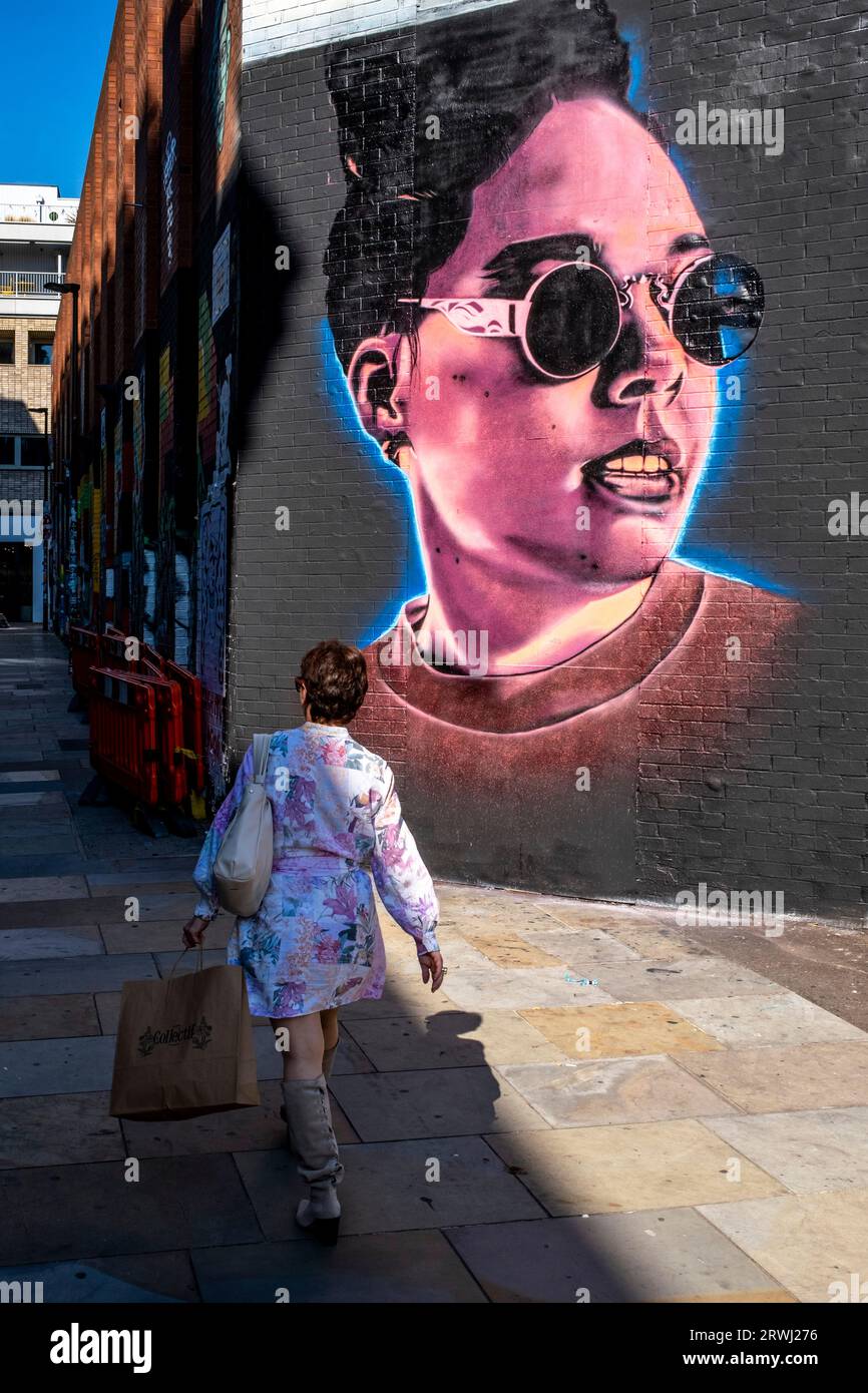 Una donna cammina davanti a un po' di colourful Street Art, Shoreditch, Londra, Regno Unito. Foto Stock