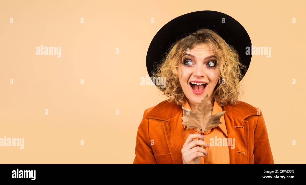 Donna autunnale con cappello nero, giacca arancione con foglia d'acero che guarda lontano. Modello femminile alla moda in abiti trendy con foglie autunnali. Moda autunnale per Foto Stock