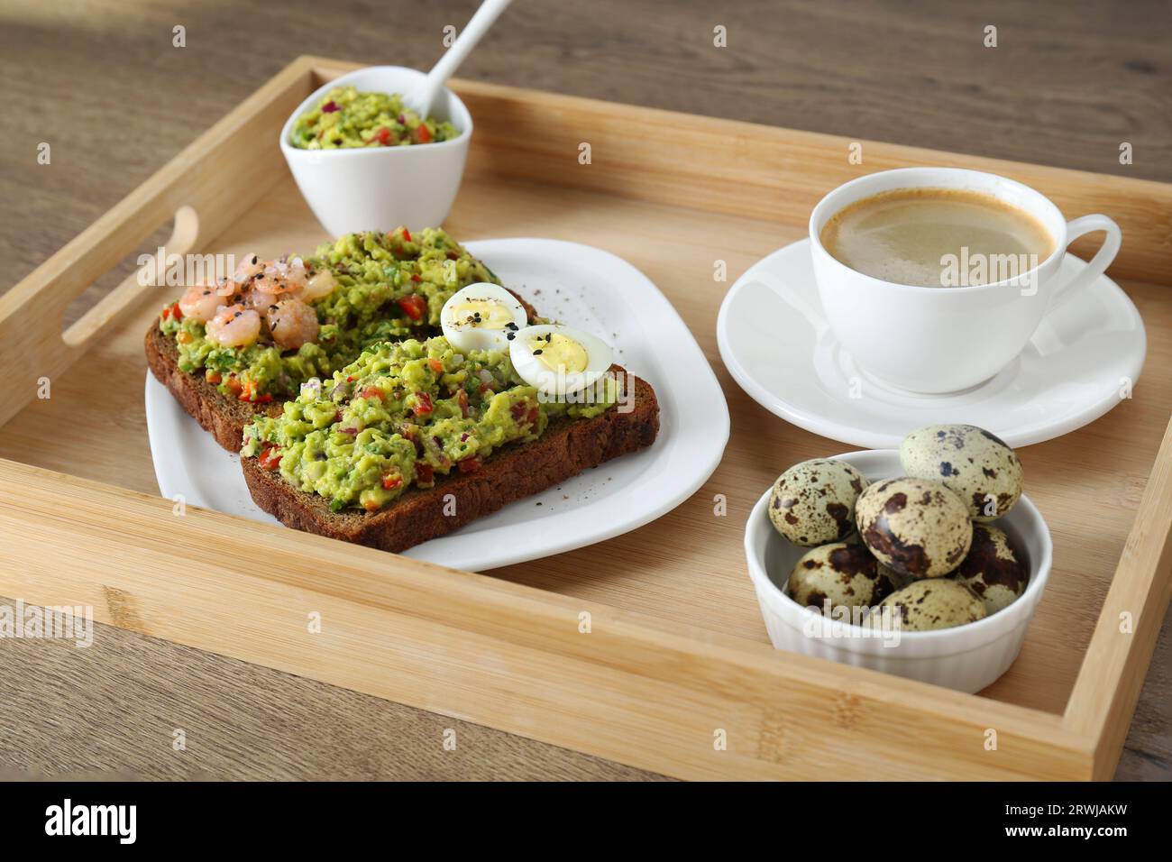 Fette di pane con guacamole, uova, gamberi e caffè su un tavolo di legno Foto Stock