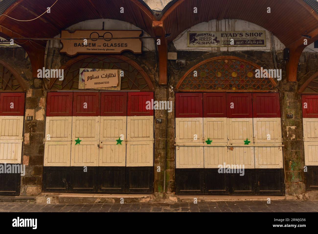 Ottico sulla vivace via al Nawfara, una delle principali aree commerciali della vecchia Damsco, in Siria. Negozi chiusi, falchi nazionali dipinti sulle porte Foto Stock