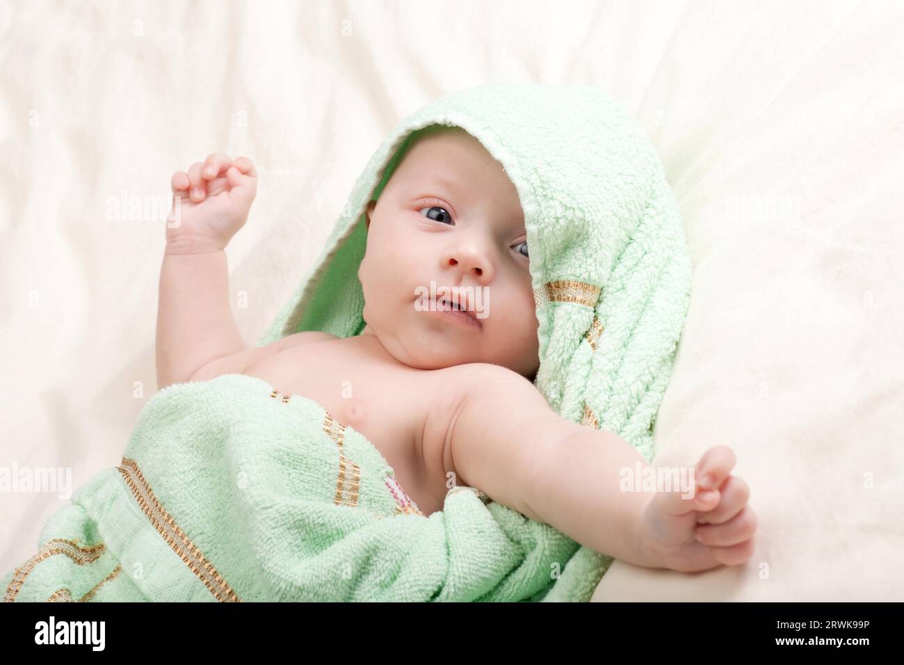 Dieci settimane vecchio incantevole piccola bambina bimbo avvolto in asciugamano stretching le braccia Foto Stock