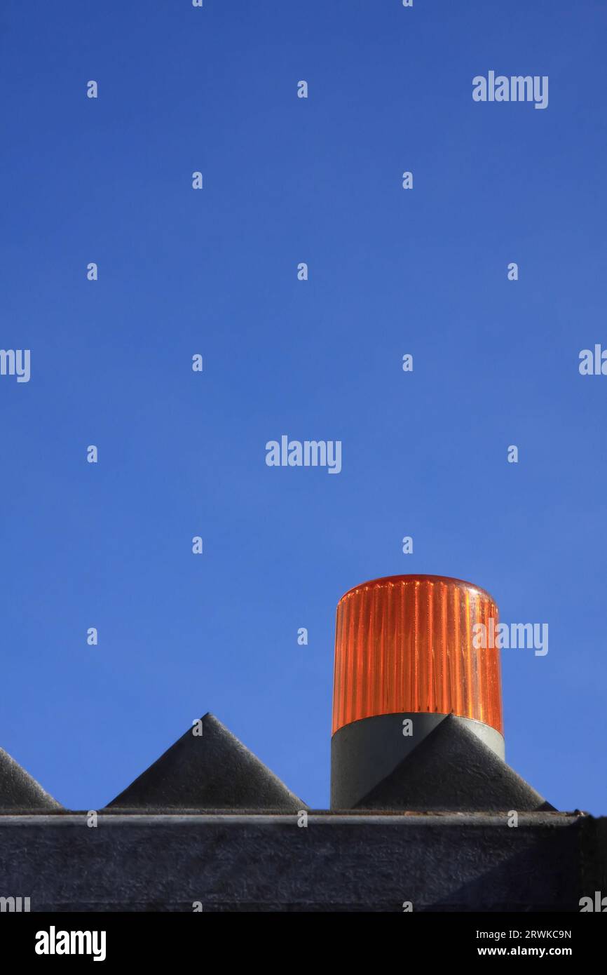 Spia di colore arancione davanti a una recinzione di fabbrica, sfondo cielo blu brillante Foto Stock