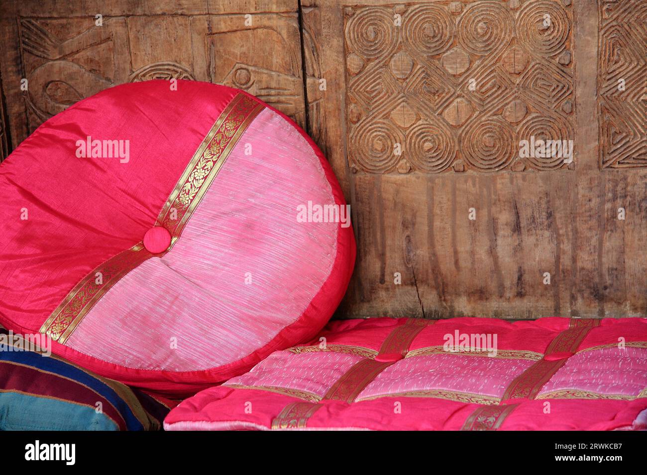 Cuscini rotondi e angolari rosso-rosa con bordi color oro invitano a sedersi, pareti in legno con ornamenti Foto Stock