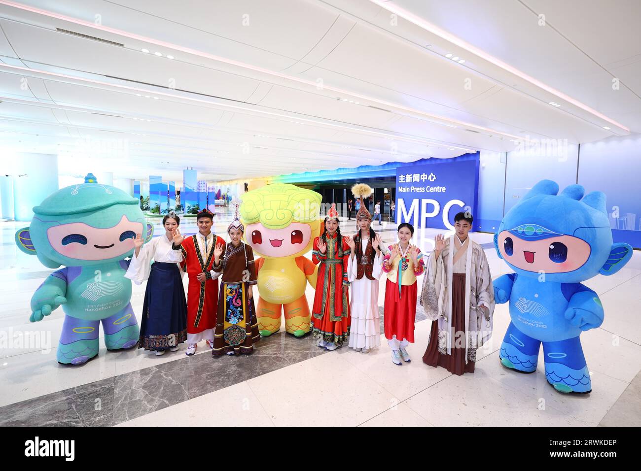 I volontari dell'Università di Zhejiang vestiti con costumi etnici accolgono giornalisti di vari paesi con la mascotte dei Giochi asiatici al Main Foto Stock