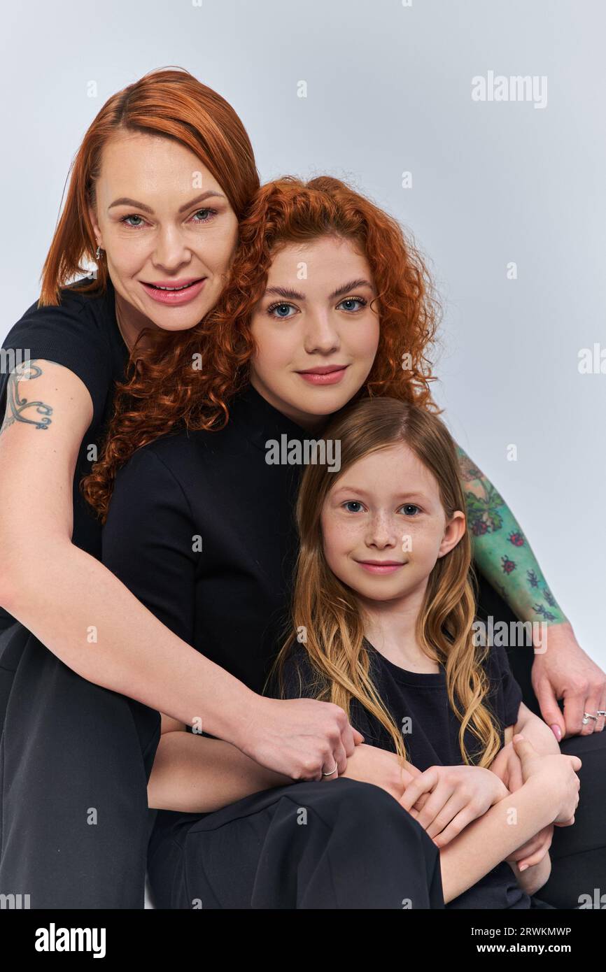 tre generazioni, allegra famiglia rossa con outfit coordinati che si abbracciano su sfondo grigio Foto Stock