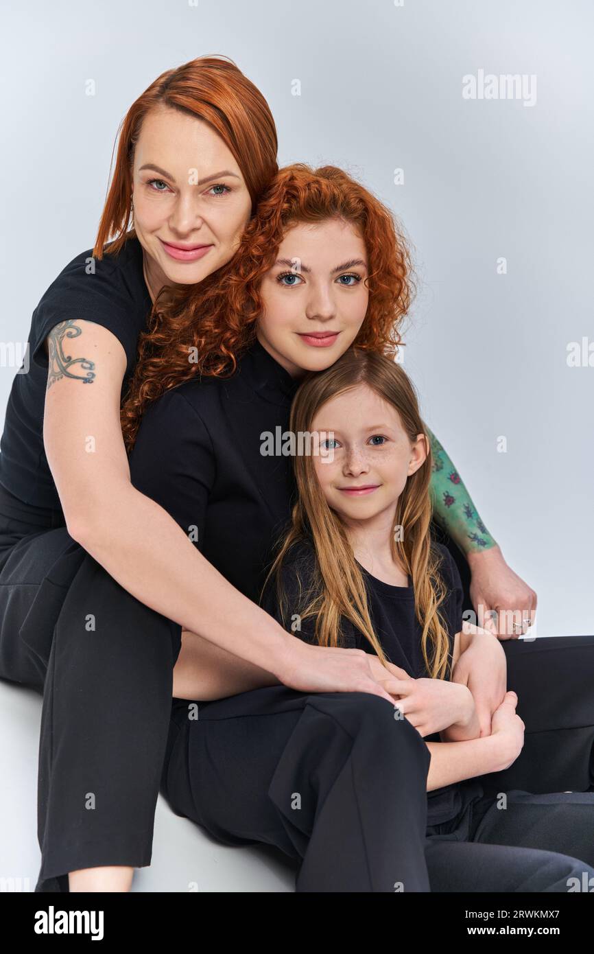 tre generazioni, gioiosa famiglia rossa in abiti coordinati che si abbracciano su sfondo grigio Foto Stock