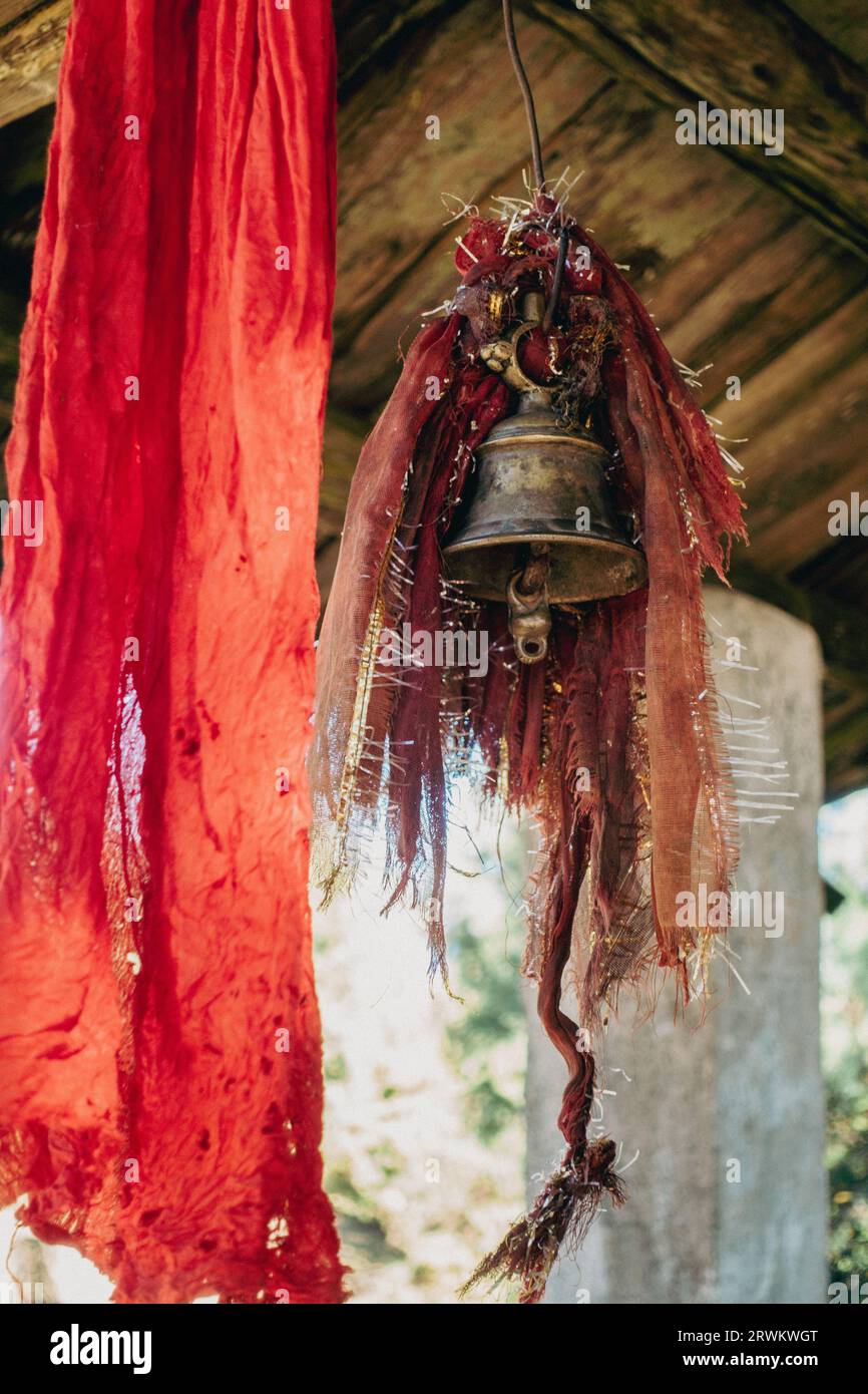Immagine in stile vintage di una campana di rame drappeggiata in tessuto rosso sacro, che adorna un tempio a Uttarakhand, India Foto Stock