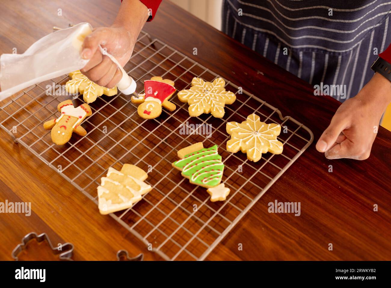 Uomo birazziale che indossa grembiule che decora biscotti natalizi in cucina Foto Stock