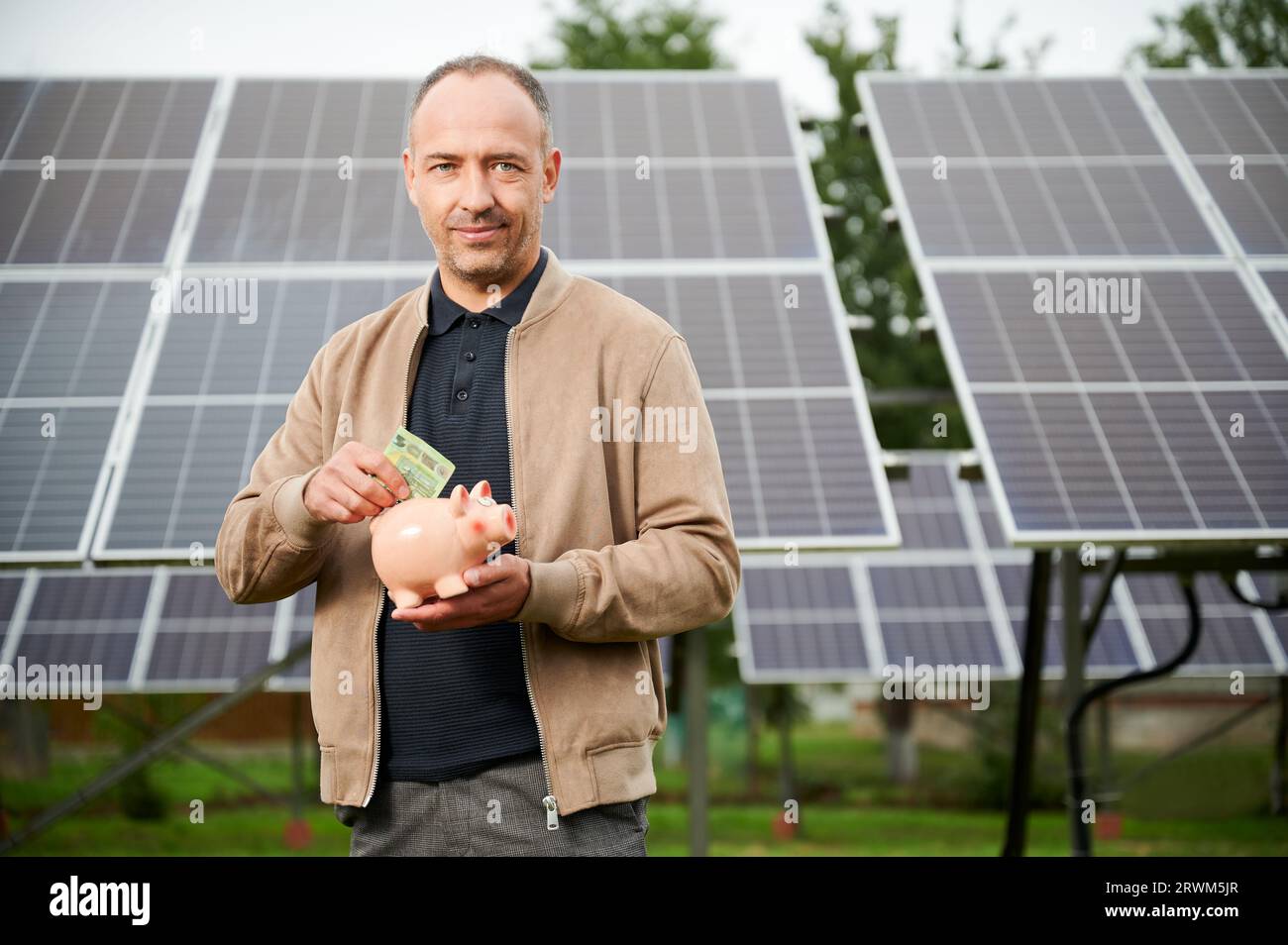 Uomo di fiducia che mette i soldi guadagnati alla banca del piggy. Il profitto di risparmio dell'adulto maschio ha ottenuto investendo nell'energia verde. Uomo in abiti casual tenendo in mano la scatola del denaro e mettere euro in esso. Foto Stock