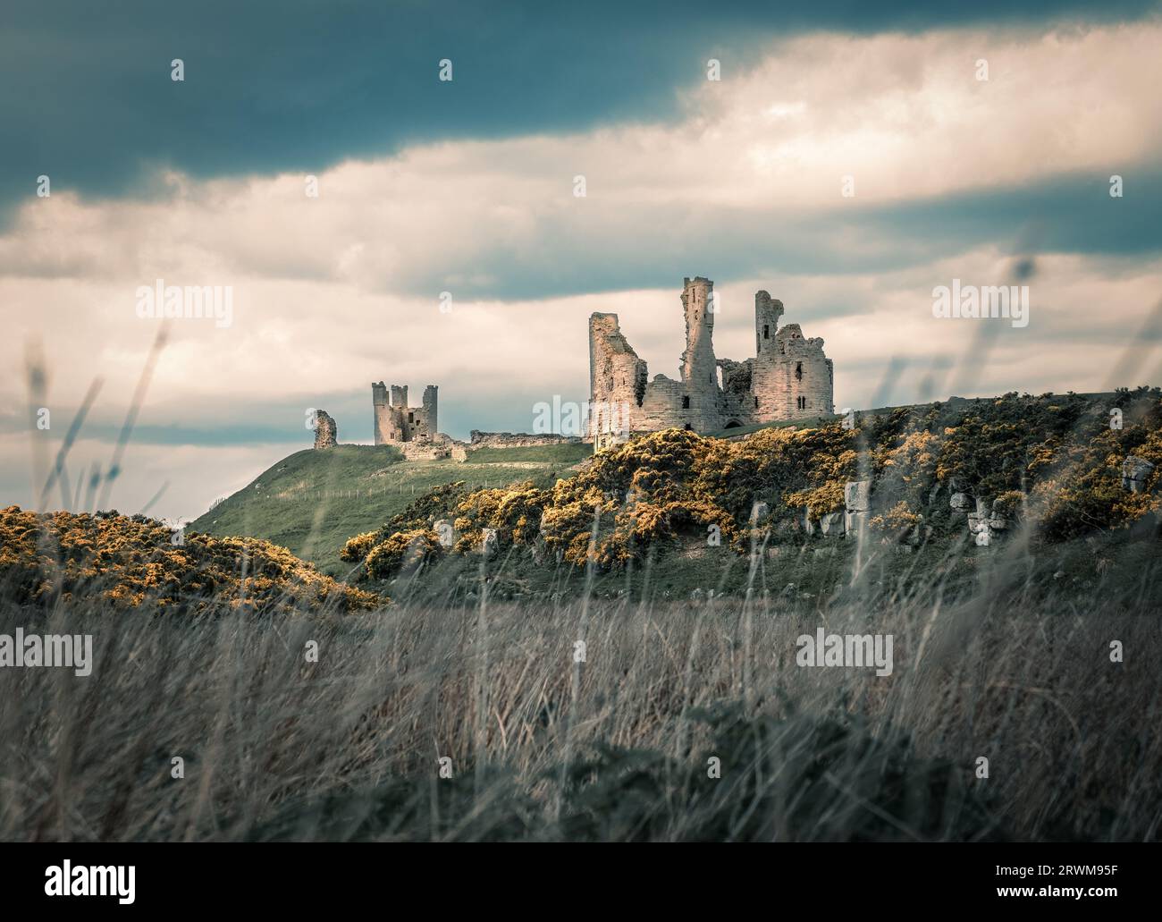 Le rovine del castello di Dunstanburgh sulla cima di una collina rocciosa con un suggestivo cielo nuvoloso Foto Stock