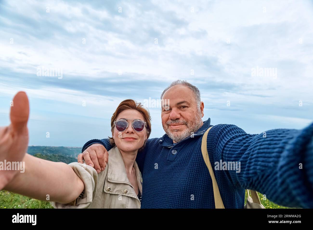 Le coppie di viaggiatori di mezza età si divertono in montagna usando lo smartphone per scattare selfie. Salute mentale, benessere, viaggio avventura e stile di vita sano. Foto Stock