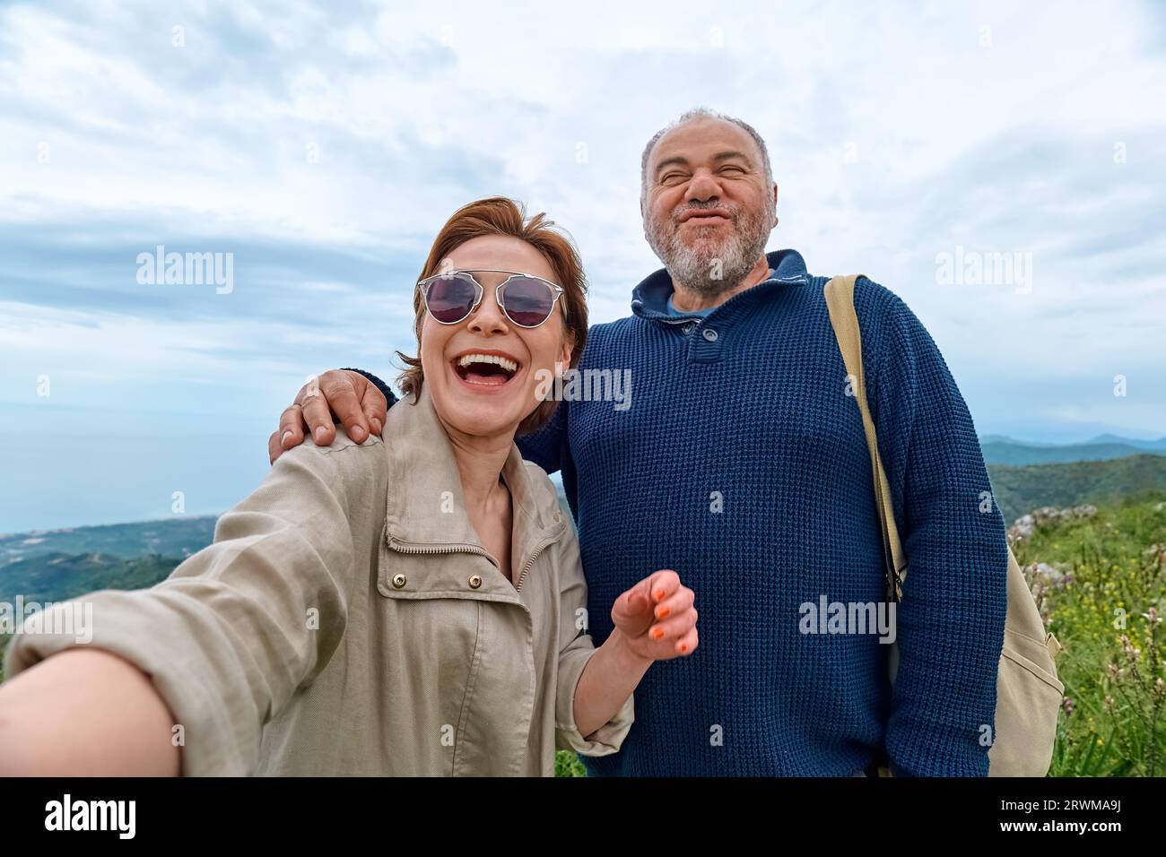 Le coppie di viaggiatori di mezza età si divertono in montagna usando lo smartphone per scattare selfie. Salute mentale, benessere, viaggio avventura e stile di vita sano. Foto Stock