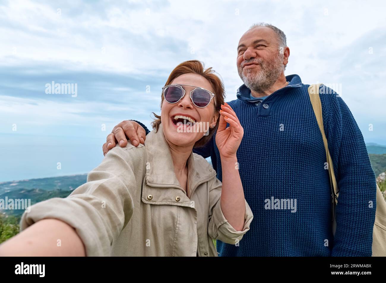 Le coppie di viaggiatori di mezza età si divertono in montagna usando lo smartphone per scattare selfie. Salute mentale, benessere, viaggio avventura e stile di vita sano. Foto Stock