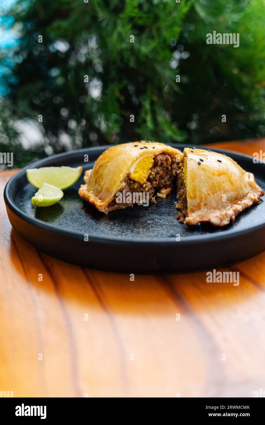 Una deliziosa empanada di pasticceria accompagnata da fette di lime fresco su un piatto bianco, pronto per essere gustato Foto Stock