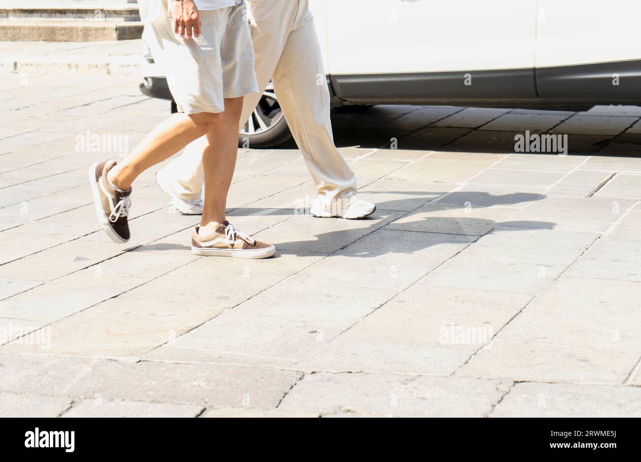 Dettaglio di due zampe di turisti mentre passeggiano per il centro storico di una città europea in una giornata di sole Foto Stock