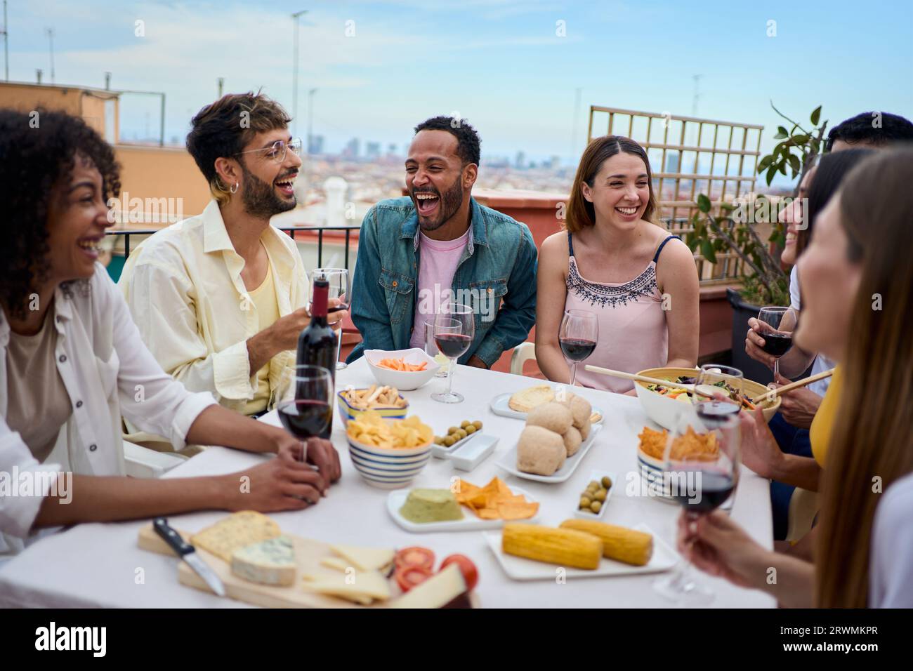 Un gruppo di giovani amici multirazziali che si divertono a pranzare insieme all'aperto. Gente allegra che fa festa. Foto Stock