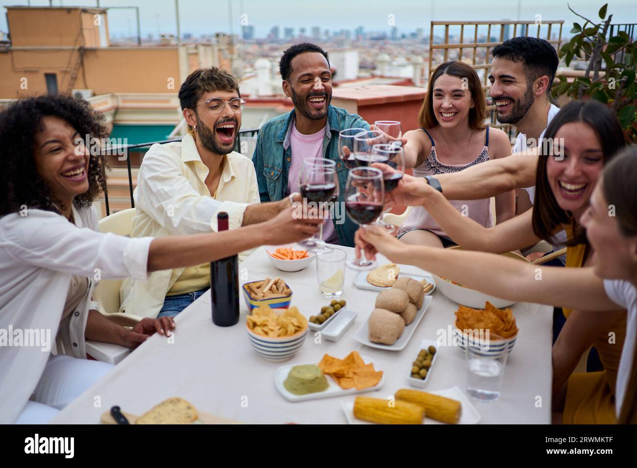 Raduna allegri giovani amici multirazziali, brinda vino rosso e festeggia sul tetto. Foto Stock