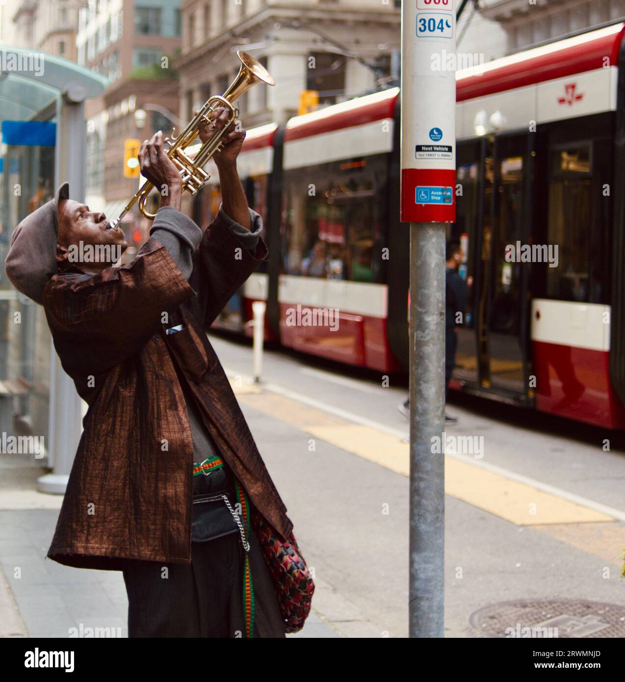 Un giovane musicista maschio adulto che suona una tromba in una fermata dell'autobus in un ambiente urbano. Foto Stock