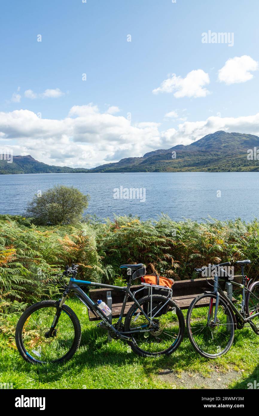 Mountain bike appoggiate su una panchina sul Loch Katrine nel Parco Nazionale del Trossachs, Stirling, Scozia Foto Stock