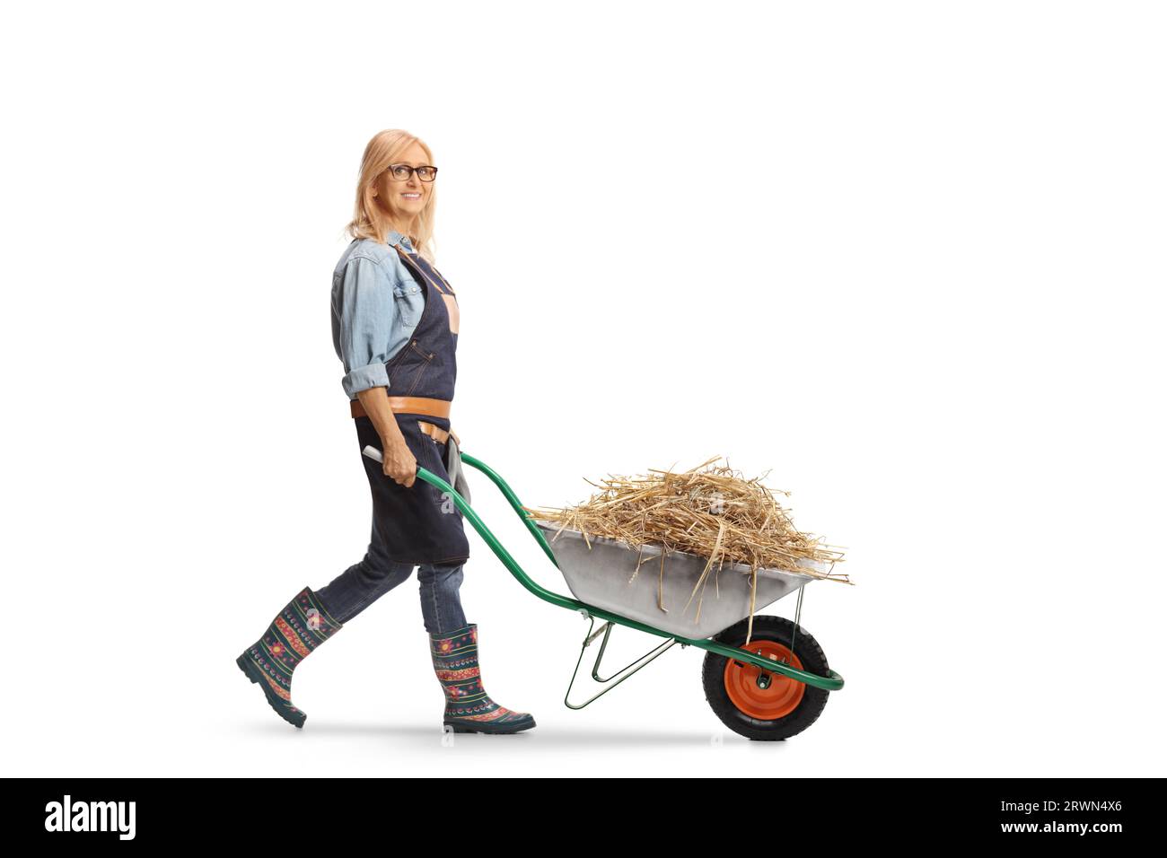 Foto a lunghezza intera di una donna contadina che cammina con il fieno in una carriola isolata su sfondo bianco Foto Stock