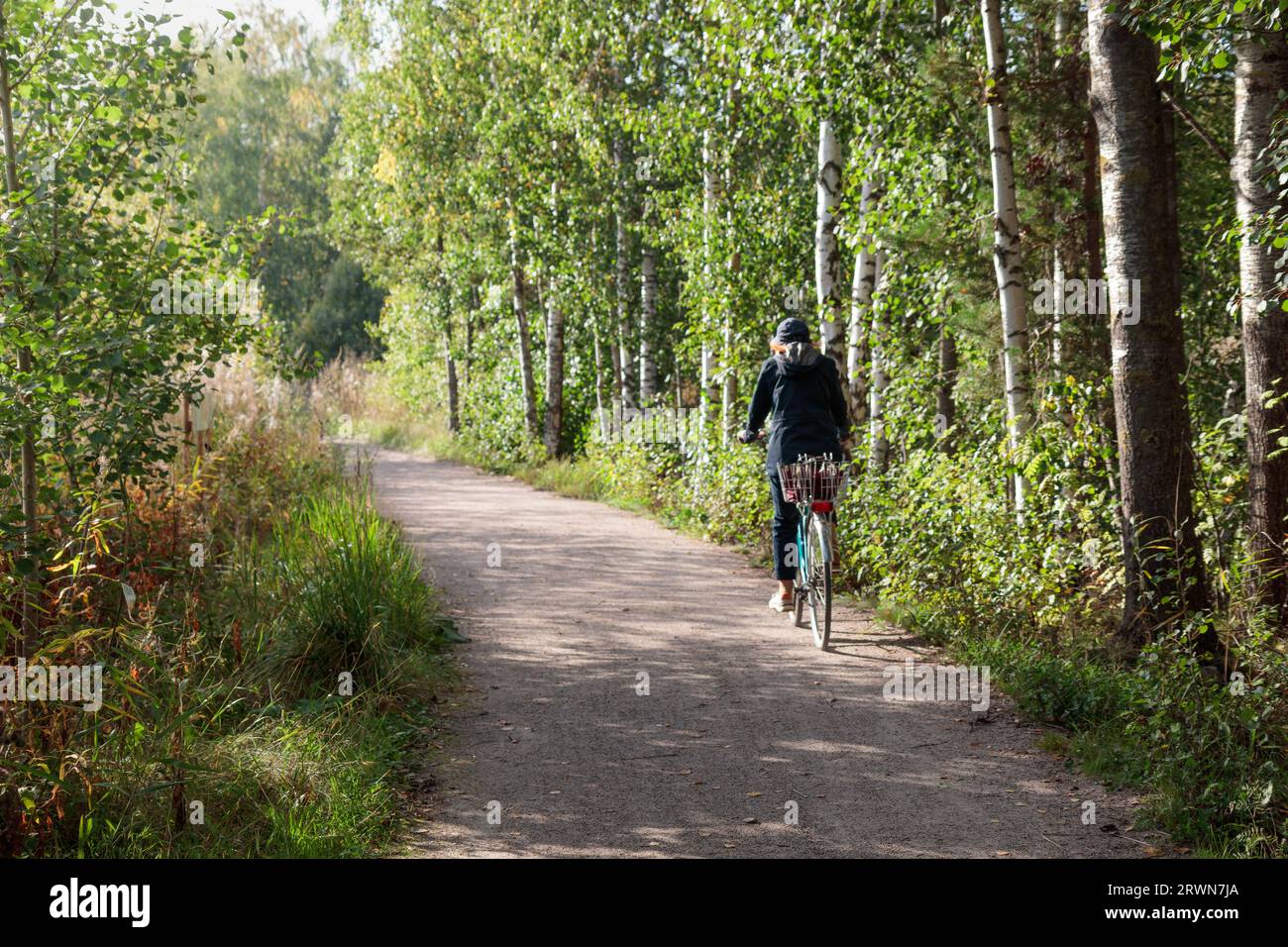 Espoo, Finlandia, 09.09.2023 - Bikepacking donna in bicicletta su strada forestale circondata da alberi, Suomenoja Foto Stock