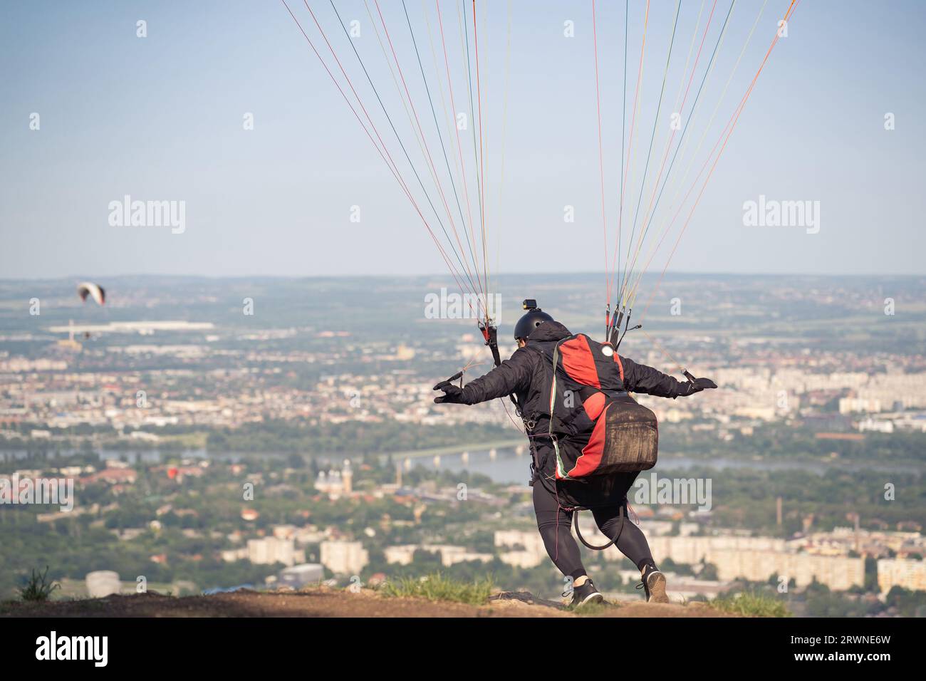 Un parapendio sta per correre per prendere il vento e unirsi agli altri in aria. Paesaggio urbano sullo sfondo. Foto Stock