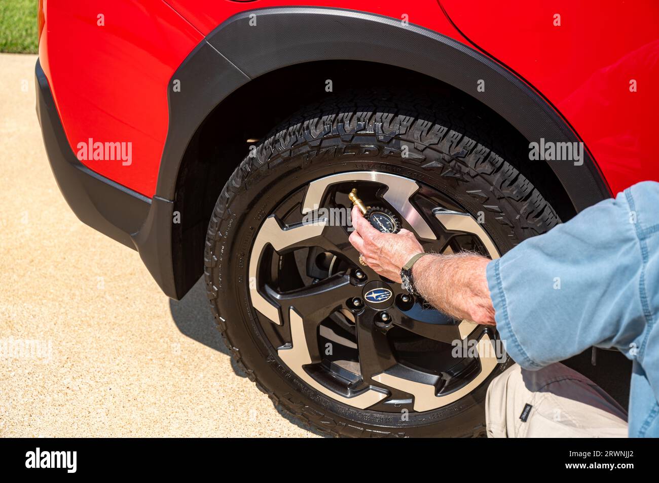 Uomo anziano adulto che controlla la pressione degli pneumatici tenendo in mano un manometro o una riparazione automatica fai da te. Foto Stock