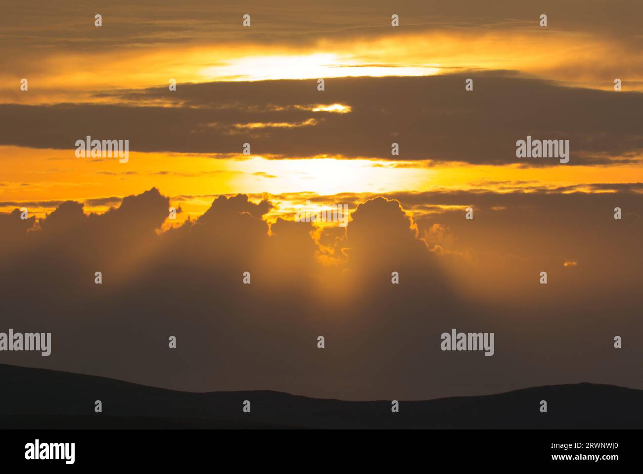 Bagliore arancione di sole che tramonta dietro le nuvole Foto Stock