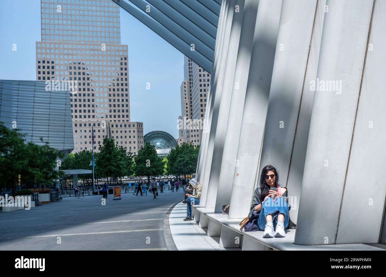 USA, New York, City, donna seduta all'edificio Oculus e con il cellulare, skyline urbano alle spalle Foto Stock